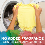 Hands holding a yellow baby onesie in front of a washing machine with 'NO ADDED FRAGRANCE' text and colorful paint splash