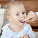Parent using a clear silicone finger brush to clean a smiling baby’s mouth in a home setting