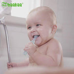 Smiling baby chewing on a translucent Haakaa 360 silicone toothbrush while sitting in a tub