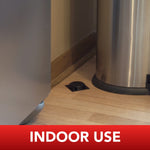 Black ant bait station placed on a kitchen floor corner next to a stainless trash can with “INDOOR USE” banner