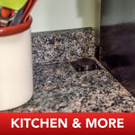 Ant bait station positioned on a granite kitchen countertop near a utensil holder with a “KITCHEN & MORE” banner