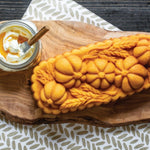 Baked golden loaf with pumpkin and wheat pattern on wooden board beside jar of whipped butter