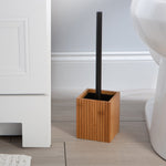 Bamboo square toilet brush holder with black-handled brush placed on a bathroom floor next to a toilet and cabinet