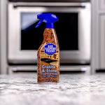 Bar Keepers Friend Granite & Stone spray bottle standing on a granite countertop with a blurred kitchen oven in the background.