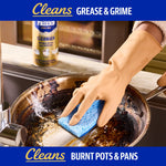 Close-up of gloved hand scrubbing a heavily burnt pan with a blue sponge and Bar Keepers Friend can blurred in background.