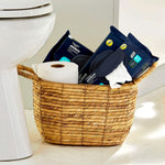 Wicker bathroom basket holding three packs of Equate flushable wipes and a toilet paper roll next to a toilet.