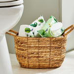 Wicker basket in bathroom holding two Equate flushable wipes packs and a toilet paper roll near a toilet.