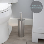 Stainless steel toilet brush holder placed on a bathroom floor next to a toilet and vanity