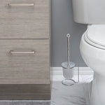 Chrome-handled toilet brush in frosted plastic holder on a chrome ring stand placed next to a toilet and cabinet