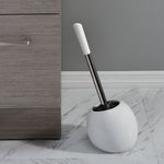 Bath Bliss white dome toilet brush and holder placed on marble floor beside gray cabinet