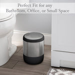 Stainless and black round waste bin placed on a bathroom floor next to a toilet, styled lifestyle image emphasizing compact fit.