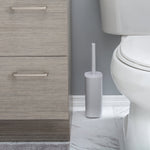 White toilet brush and rectangular holder placed on bathroom floor between vanity and toilet in a staged bathroom scene