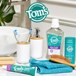 Bathroom counter scene showing a tube of Tom's toothpaste, mouthwash, deodorant, brushes, and Tom's logo above on a vanity setting.
