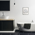 Bathroom lifestyle scene with a framed Stupell print featuring a toilet-paper illustration and the phrase 'Text me if you need anything' hung above a bathtub.