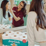 Bathroom mirror scene with an AngelSoft pack of toilet paper on the counter and people interacting reflected in the glass