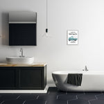 Modern bathroom scene with a framed farmhouse truck print hung above bathtub and sink on a white wall.