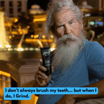 Bearded man holding a black tube of Grind toothpaste in a night-time outdoor scene with warm bokeh lights behind him