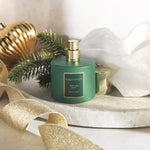 Styled scene of BEAUTYSPACE Winter Pine room spray bottle with removed cap, evergreen sprig and gold ribbon accents