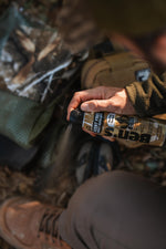 Close-up of hand spraying a Ben's scent free hunting formula aerosol can, mist visible over boots and outdoor gear
