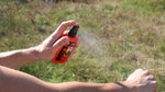 Person spraying an orange Ben's insect repellent pump bottle onto their forearm in an outdoor grassy area