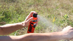 Close-up of a hand spraying Ben's tick repellent onto a forearm outdoors, visible mist from the can.