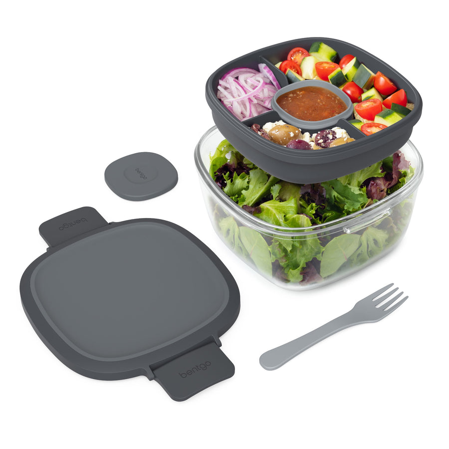 Dark gray Bentgo glass salad container with clear bowl, compartmented tray holding salad ingredients, lid, fork, and sauce cup