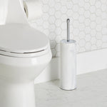 Bathroom scene with white faux marble toilet brush and holder placed beside a toilet on tiled floor