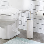Toilet brush in a white faux marble cylindrical holder positioned next to a toilet and toilet paper