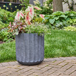 Charcoal fluted planter placed on a brick patio filled with mixed foliage and white flowers