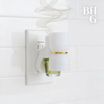 Plug-in diffuser inserted in an outlet with a glass oil bottle and stylized scent vapor, BHG logo in corner