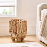 Empty twisted water hyacinth round planter placed on a hardwood floor next to a cushioned chair