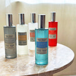Group of five Better Homes & Gardens room sprays on a marble table with the Oceanside Flannel bottle front and center