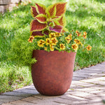 Rust-finish planter placed on a paved path filled with mixed flowering and foliage plants in a garden