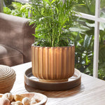 Styled scene showing a decorative ribbed planter sitting on a gray-brown Better Homes & Gardens ceramic saucer on a wooden table.