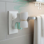 White plug-in diffuser inserted into a wall outlet with a small turquoise refill bottle attached and BHG logo in corner.