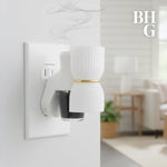 White plug-in fragrance diffuser inserted in a wall outlet with small oil bottle attached, living room background