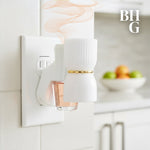 Styled kitchen scene showing a plug-in diffuser releasing fragrance from a Better Homes & Gardens refill bottle in a wall outlet