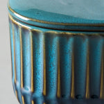 Close-up detail of teal ribbed ceramic candle container showing glaze texture and lid edge