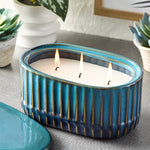 Teal ribbed oval ceramic candle burning three wicks on a tabletop with small succulents nearby