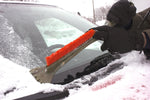Person using a black snow brush with orange bristles to clear snow from a car windshield