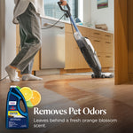 Person using a BISSELL multi-surface cleaner in a kitchen with orange slice graphic and product bottle inset labeled 'Removes Pet Odors'