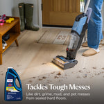 Upright BISSELL cleaner used on a wood floor with dirt and small product bottle inset plus 'Tackles Tough Messes' text