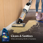 BISSELL floor cleaner machine cleaning a spilled mess on a hard floor with product bottle inset and 'Cleans & Sanitizes' text