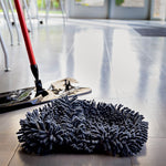 Black chenille microfiber mop head lying on a floor with a mop base and red handle in background