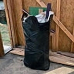 Tall black trash bag or liner standing upright inside a wooden framed room or construction area
