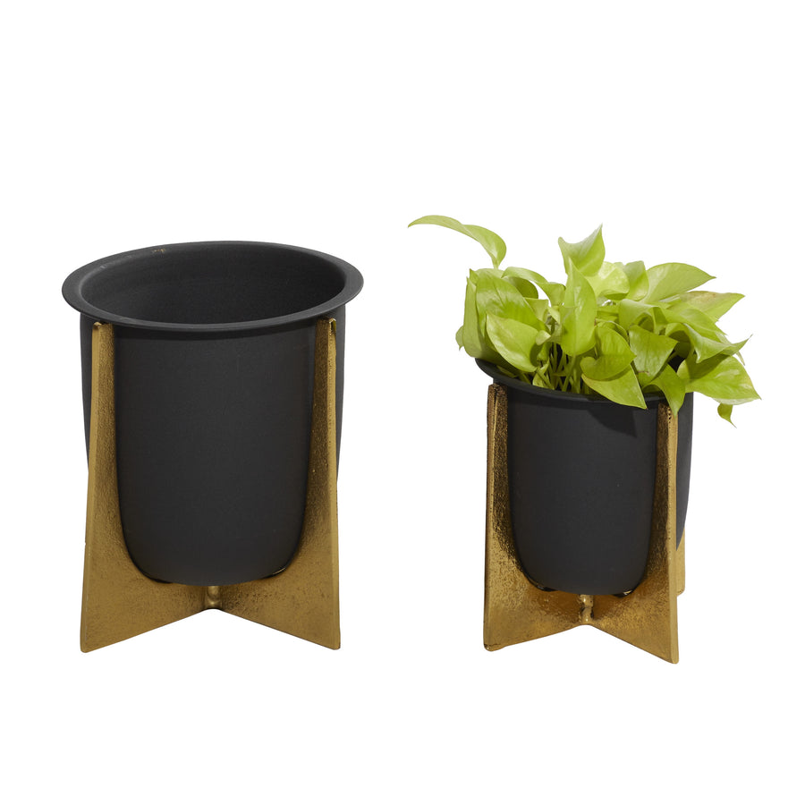 Two black metal planters with removable textured gold crisscross stands, one filled with a green trailing plant, on white background.