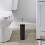 Black toilet brush and holder placed on a bathroom floor next to a toilet and vanity.