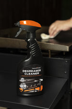 Blackstone Degreaser Cleaner bottle placed on a griddle with a hand wiping the background surface