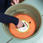 Close-up of hands placing an orange Ups-A-Daisy planter insert into a green plastic pot.