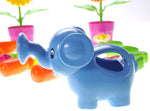 Blue plastic elephant-shaped watering can placed among toy gardening tools and potted plastic flowers on white.